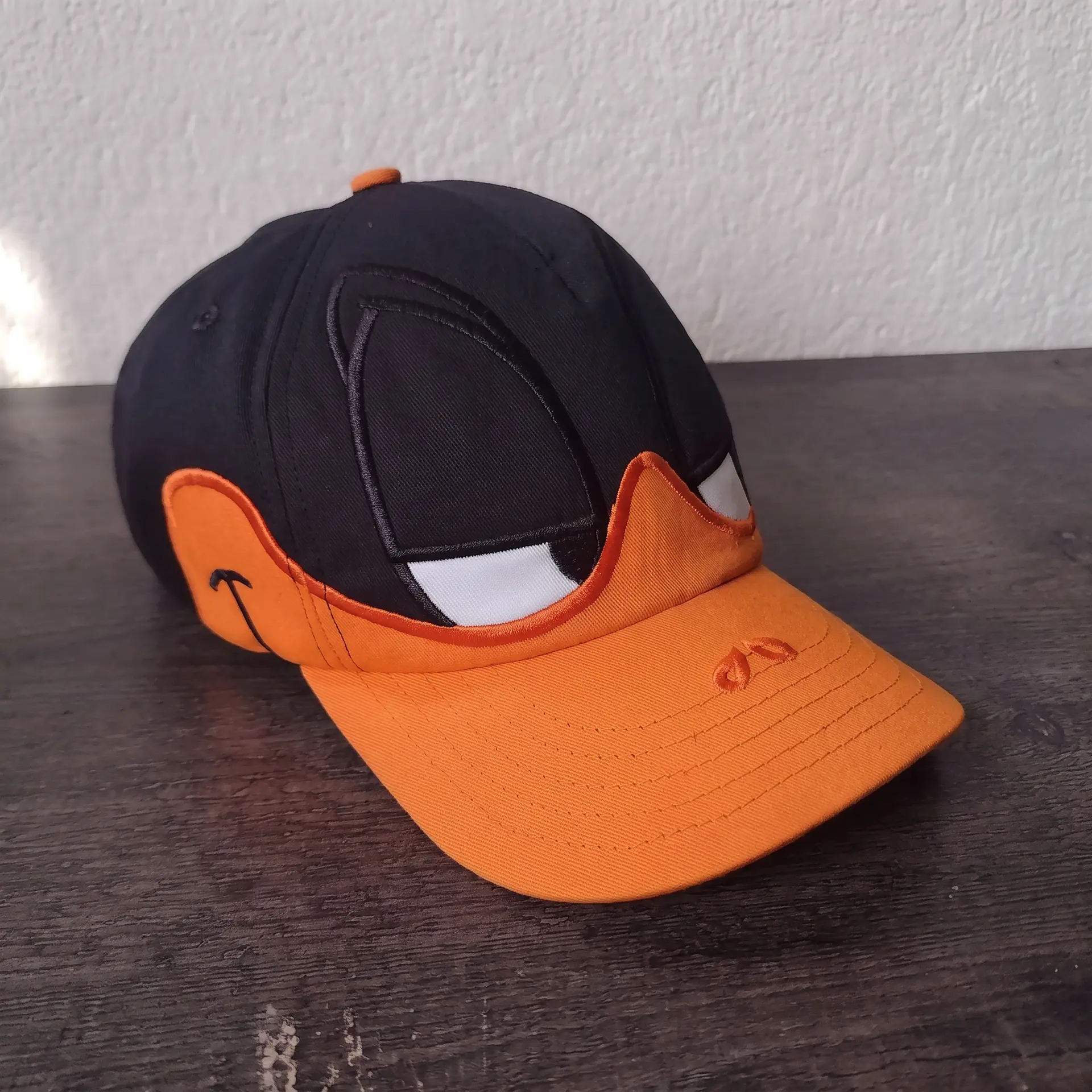 生成一张写实的产品静物摄影，主体是一顶做成达菲鸭（Daffy Duck）造型的棒球帽，放在深色木质台面上靠墙摆放。

一